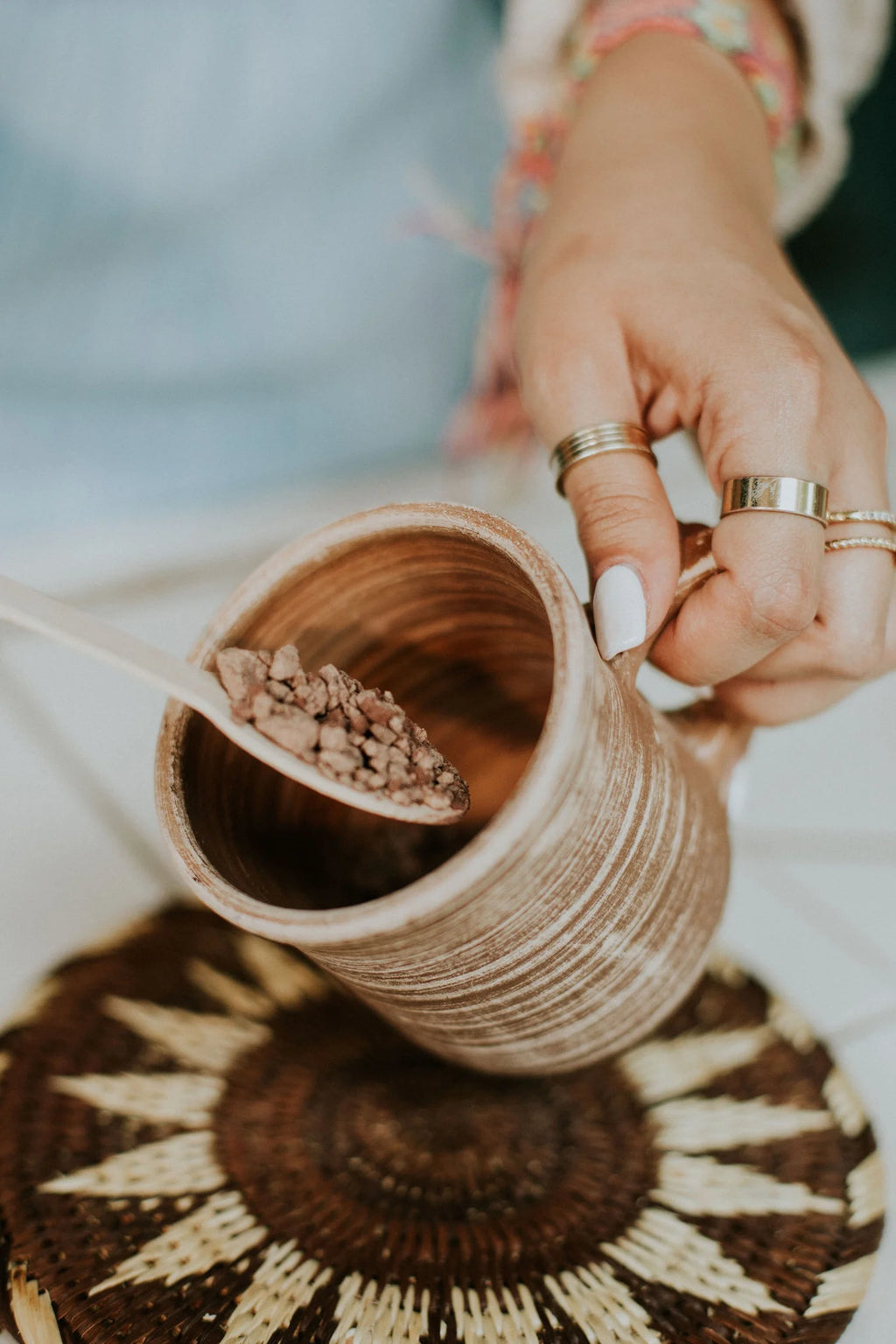 Person holding a ceramic mug with a wooden spoon holding cacao, on a textured surface.