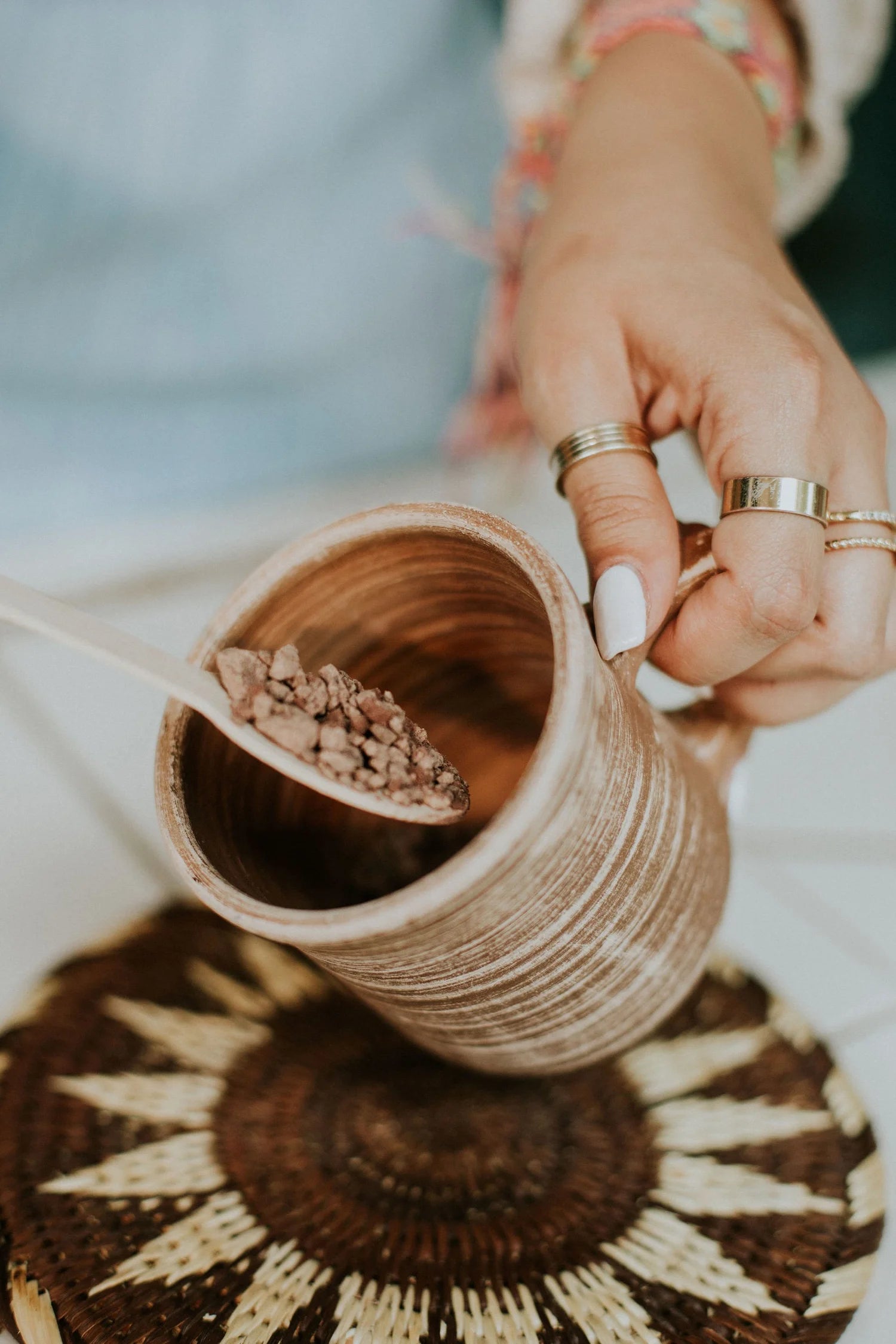 Person holding a ceramic mug with a wooden spoon holding cacao, on a textured surface.